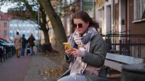 woman using a phone on a park bench in the city