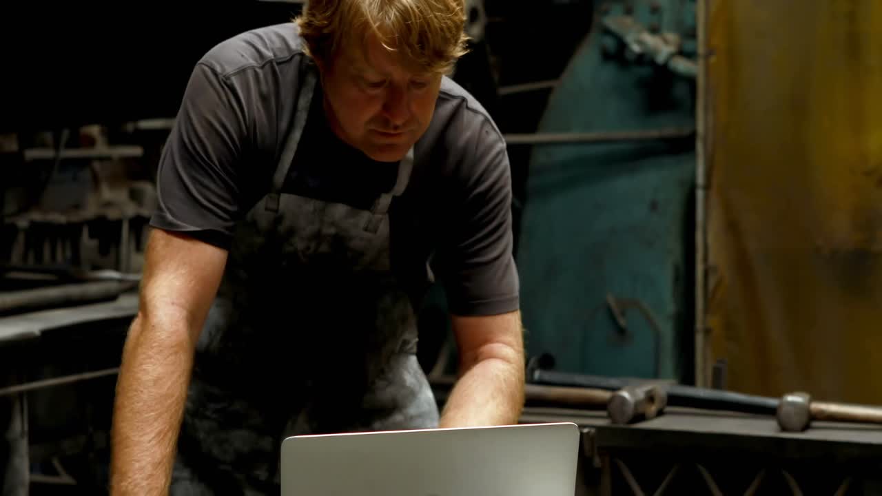 Blacksmith using laptop in workshop 4k