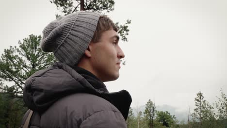 a male hiker looks around at a misty mountain landscape as rain falls around him