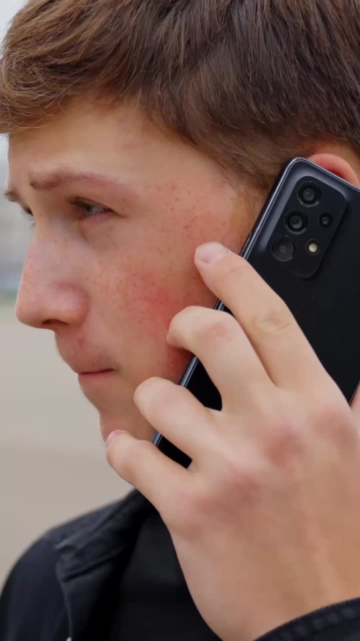 Teen boy talking on cellphone outdoors, focused and thoughtful mood