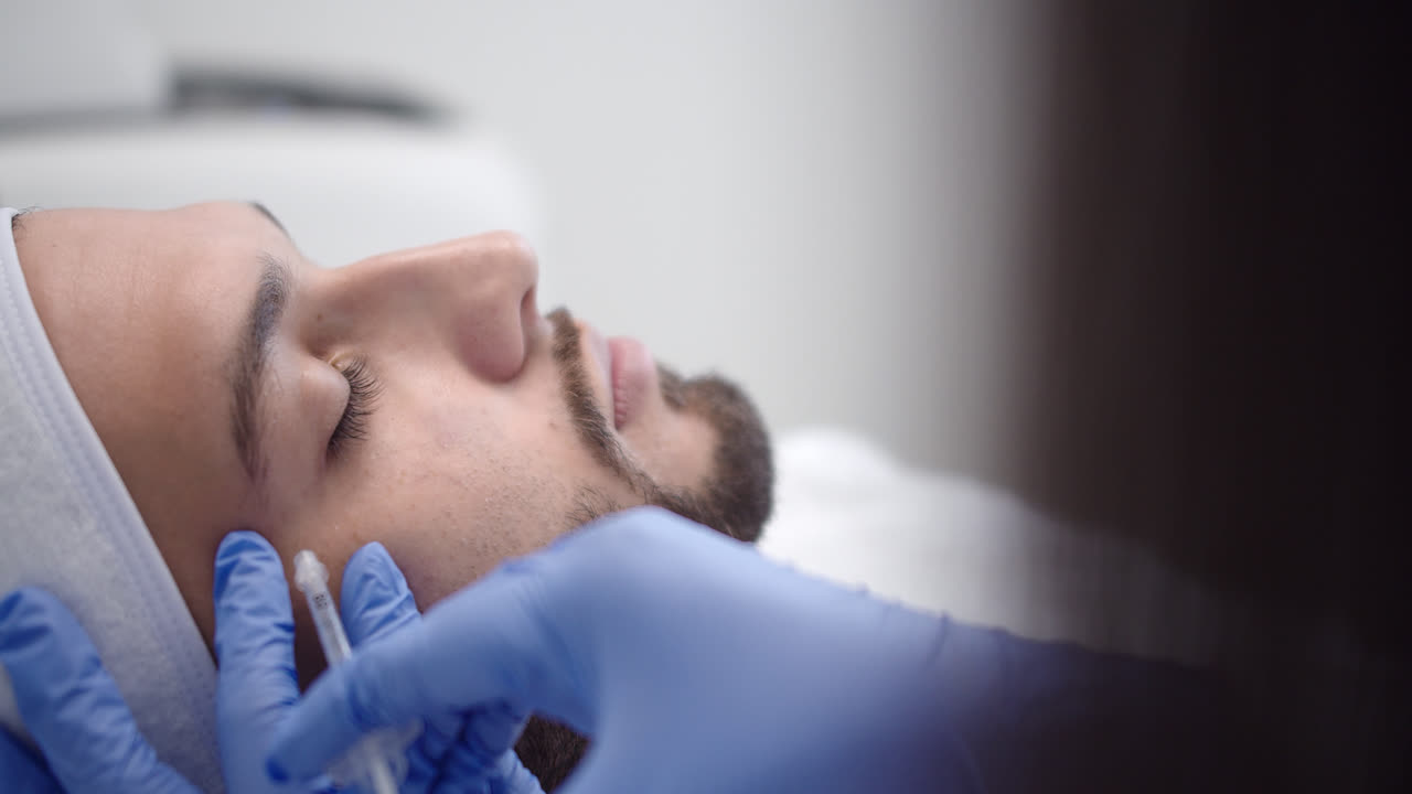 Beautiful slow motion shot of a handsome young Latino man getting injected in the face inside a dermatology clinic in a beauty treatment