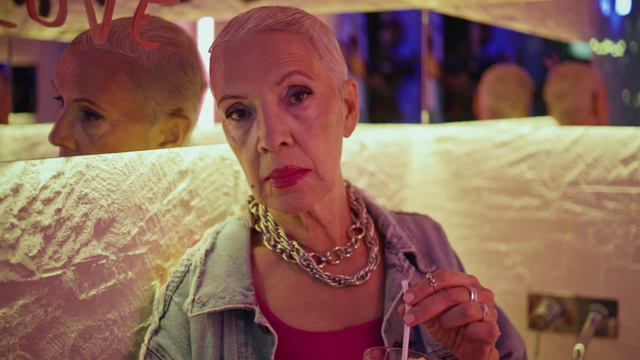 Retired woman holding cocktail in stylish outfit closeup. Serious model posing