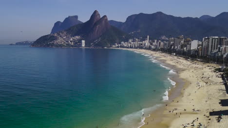 drone flying over ipanema beach rio brazil, white sandy beach, blue water, white waves, city skyscrapers, two brothers mountains background