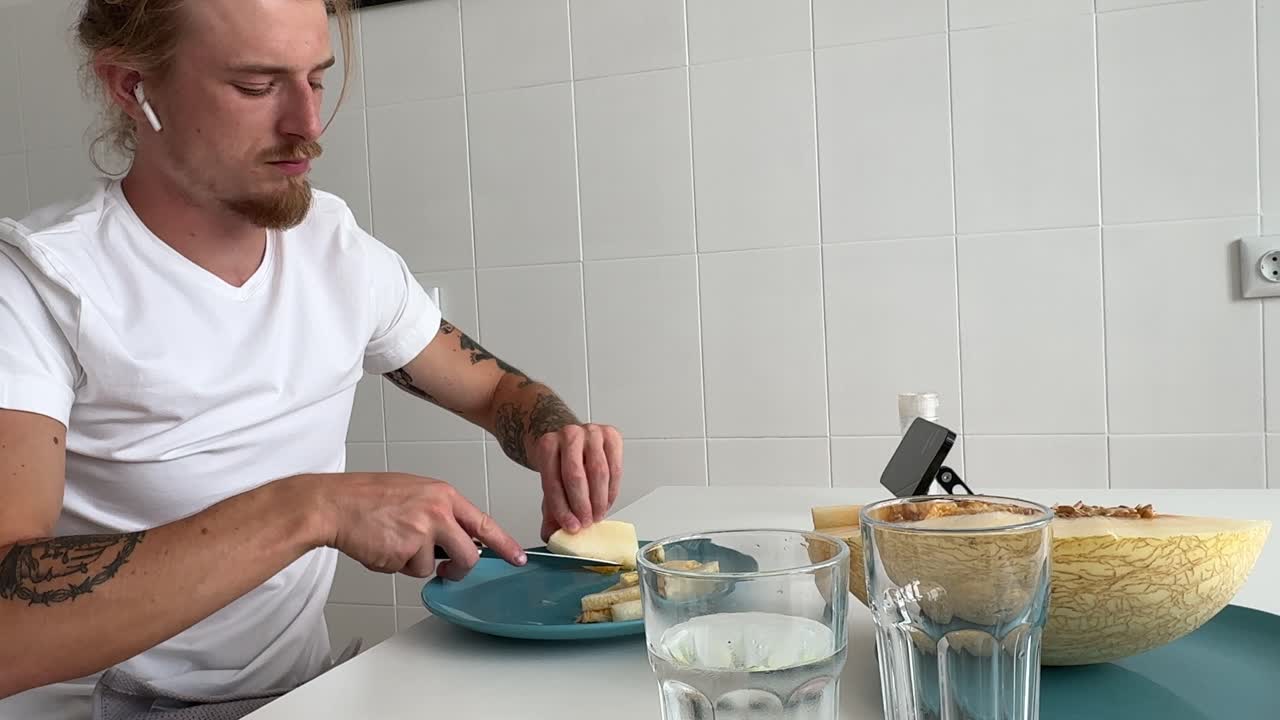 Ung mand spiser frisk melon ved køkkenbordet