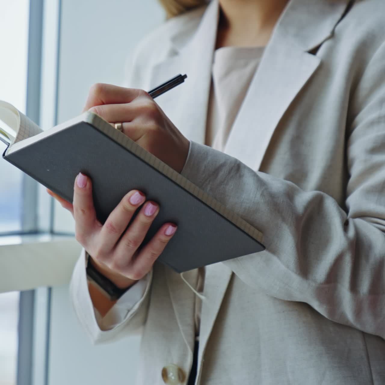 Signora in giacca leggera in piedi alla finestra che tiene in mano un quaderno. Donna che prende appunti nel suo diario. Primo piano