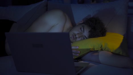 un joven se está quedando dormido mirando la computadora portátil.
