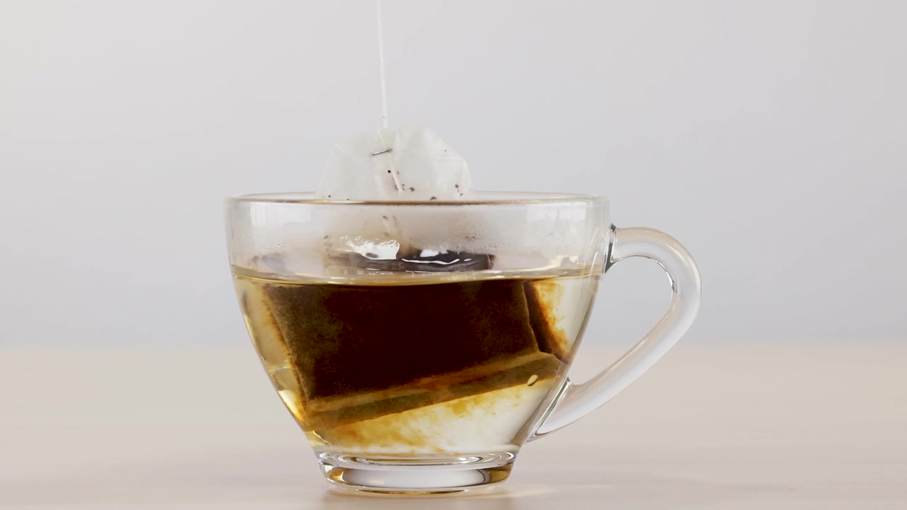 Una bustina di tè infonde acqua calda in una tazza trasparente, mostrando il liquido che si scurisce gradualmente.