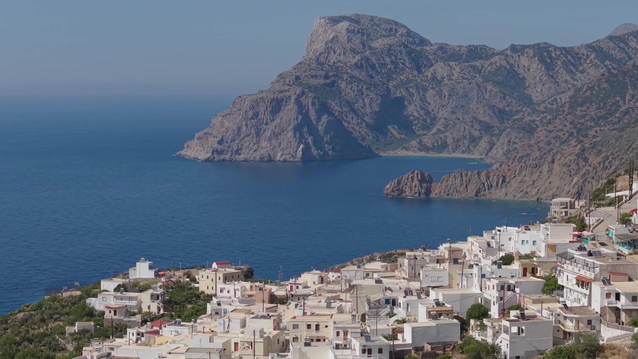 Karpathos Adası'nın engebeli dağları ve etkileyici doğal manzarasıyla çevrili Mesochori geleneksel köyünü gösteren yanal telefoto drone çekimi.