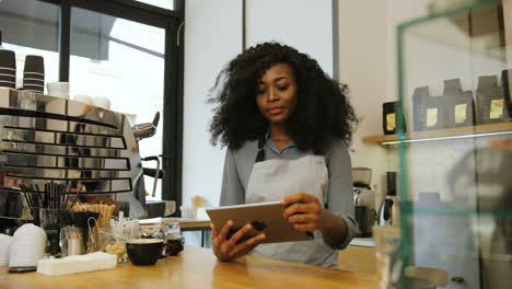 african american female barista with curly hair using a tablet in a coffee shop