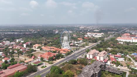 this aerial view prominently features the angkor eye, a large white ferris wheel, as a central landmark within siem reap, cambodia. stands out with its intricate structure numerous passenger gondolas.
