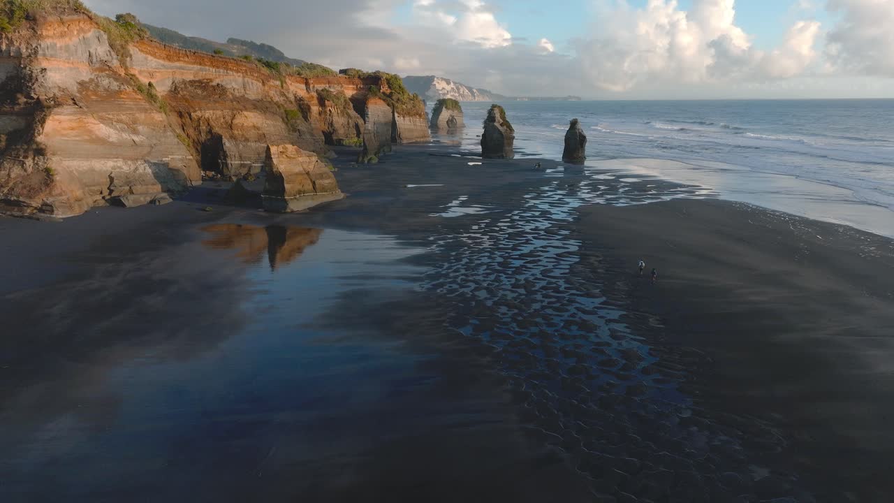 Tourists Running Towards Cliffs And Sea Stacks On Coast Of Taranaki At Three Sisters Beach, North Island, New Zealand. drone shot