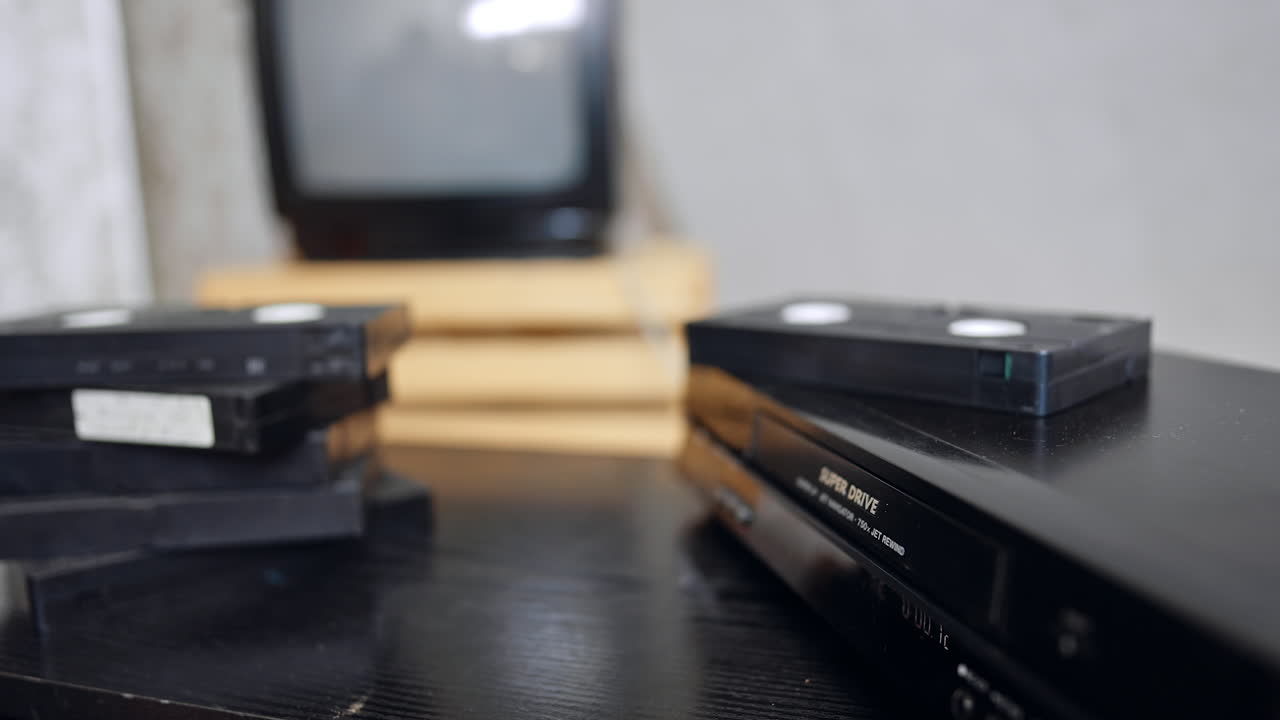 Male hand takes a VHS tape out of the player. Man puts a tape on the pile nearby. Close up
