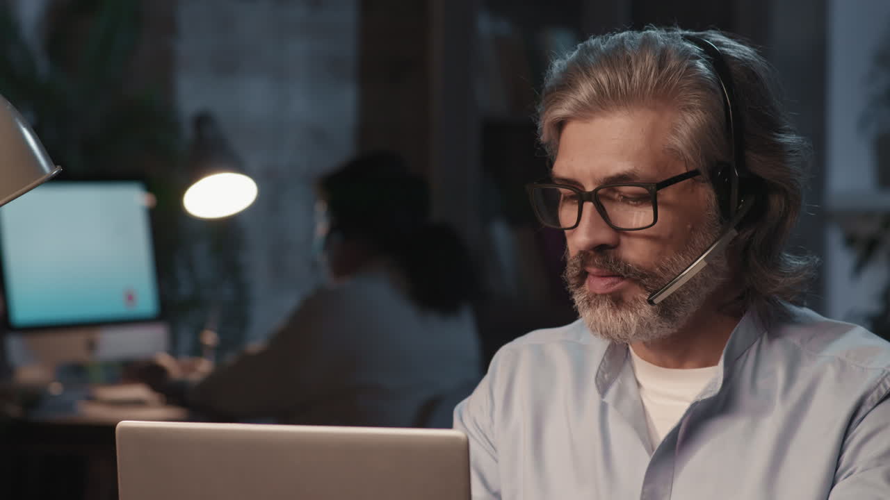 Mature Man with Headset Working on Laptop in an Office
