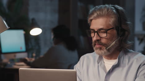 mature man with headset working on laptop in an office