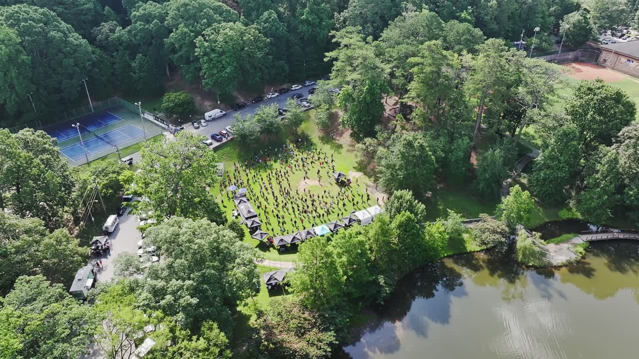 Aerial orbit showing group of people doing sport exercise on grass field of park. Sunny summer day near river in Atlanta, USA