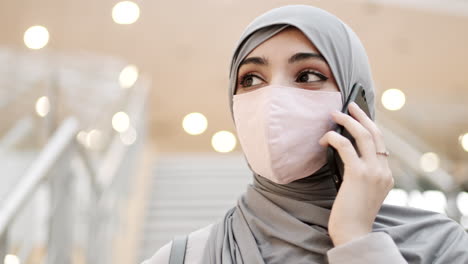 woman wearing hijab and mask talking on phone in a mall