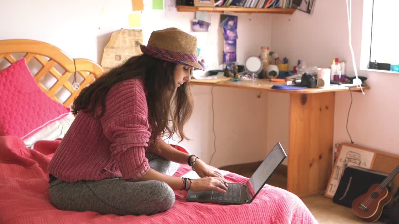 niña escribiendo en su computadora portátil sentada en la cama, en el dormitorio