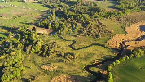 panoramic aerial of winding meander river in countryside, long shadows cast from tall trees