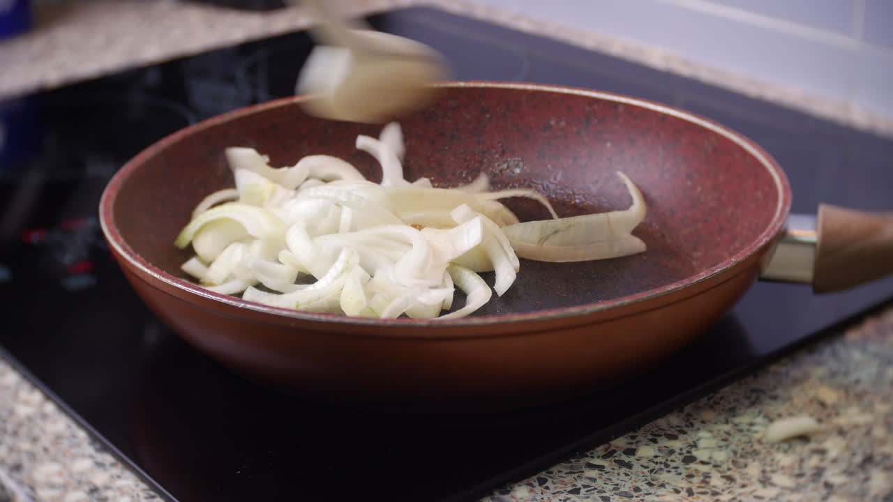 A chef stirs chopped and sliced onions in a frying pan