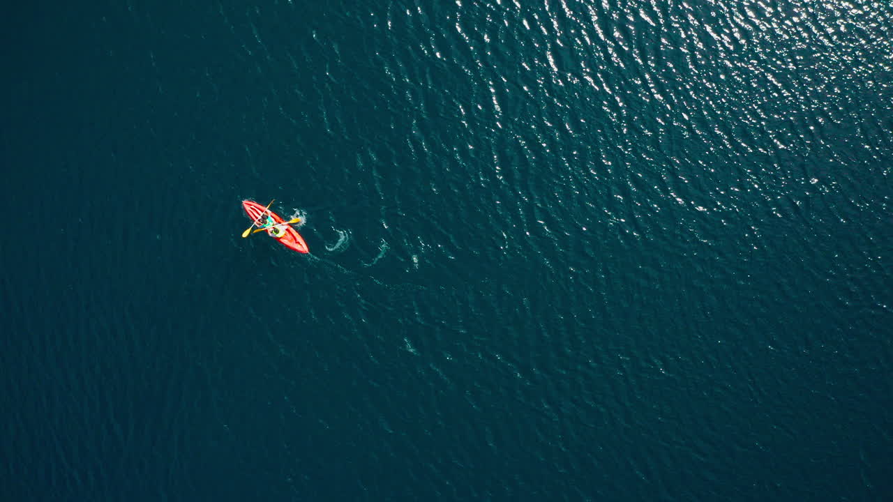 antena de arriba hacia abajo de dos personas remando kayak naranja en agua ondulada