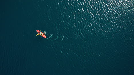 high top down aerial of two people paddling orange kayak in wavy water