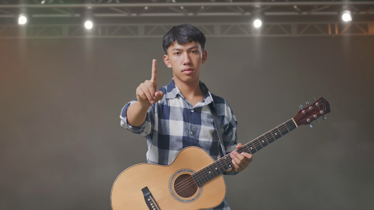 기타 를 들고 무대 에 서 있는 아시아 청소년 은 몸짓 을 보이지 않는다