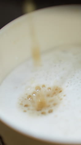 café vertiendo en una taza de una máquina de café. el video captura la vista detallada de la corriente de café mezclándose con la leche espumosa en la taza
