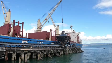 zoom in of cargo ship unloading at sugar factory time lapse as cranes work to move shipment