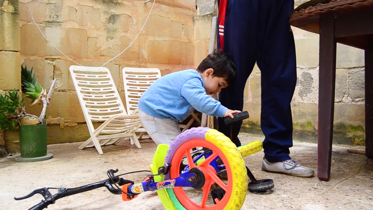 Cute male toddler playing happily with the wheels of his bicycle