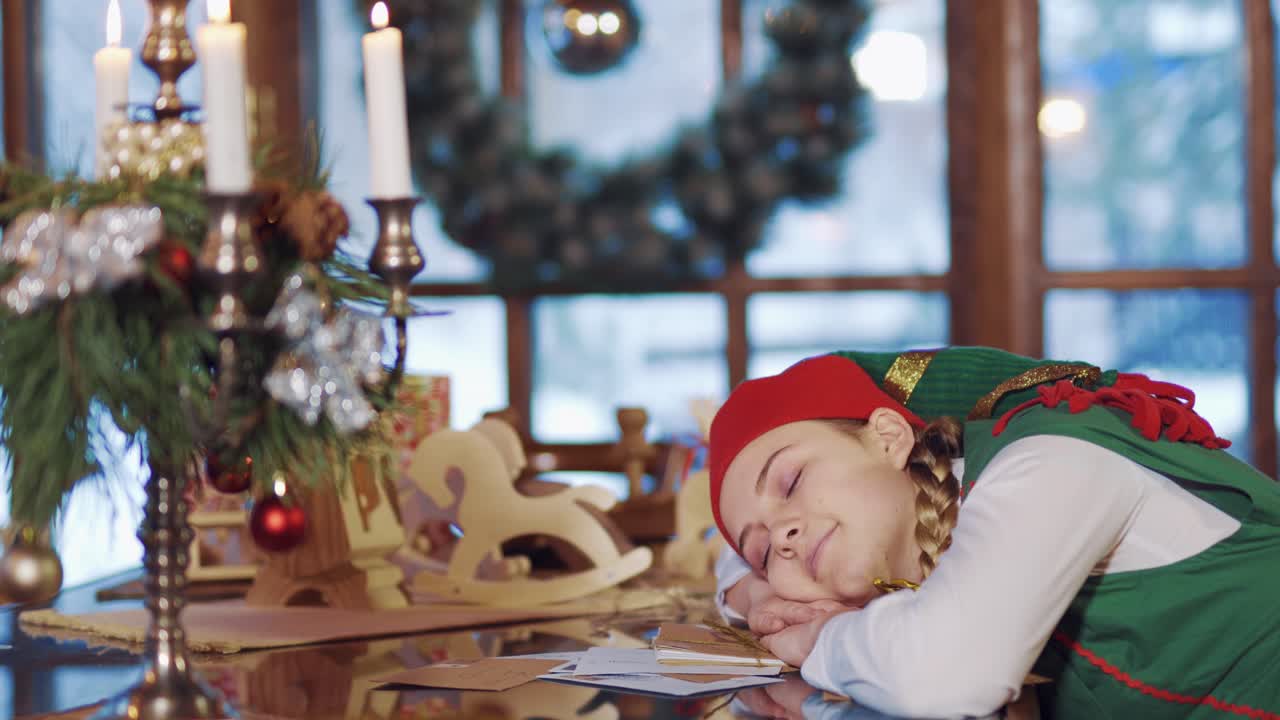Christmas time. Elf is sleeping at the table indoors. Beautiful elf wakes up after her sleep in the decorated room on festive table background.