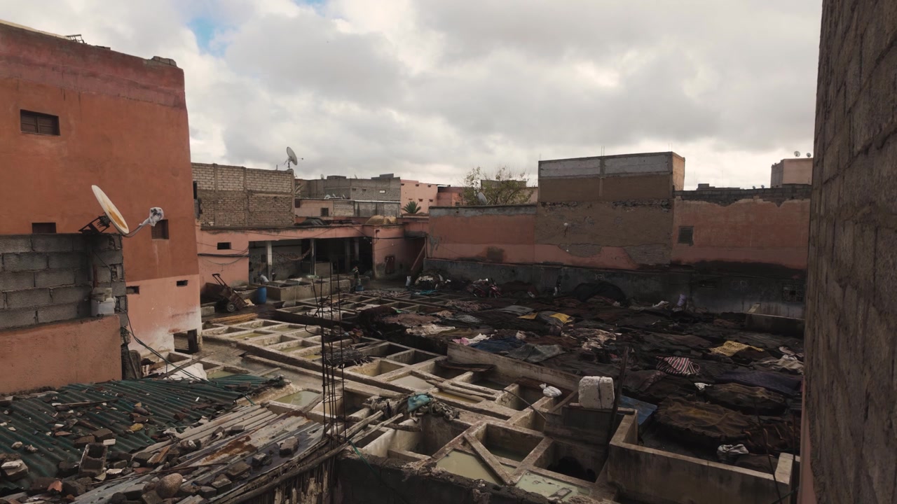 Inquadratura statica grandangolare delle concerie di Marrakech che mostra le fosse di tintura, i tetti e gli edifici in mattoni di fango rosa.
