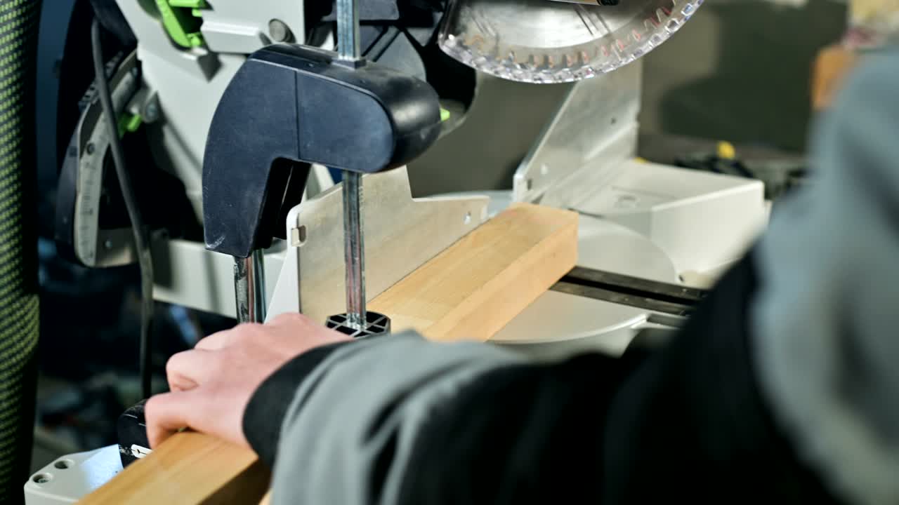 cerca de las manos del carpintero instala una pieza de madera en una sierra circular