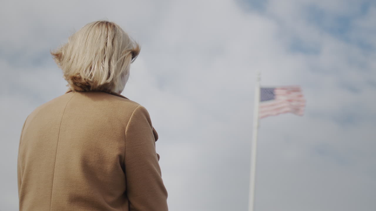 mujer mirando la bandera estadounidense en el asta de la bandera, vista trasera