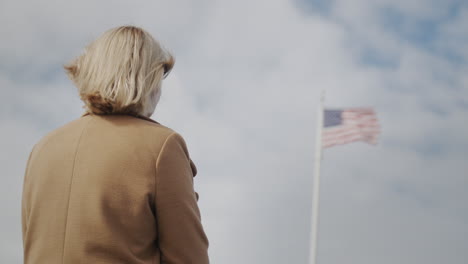 Mujer-Mirando-La-Bandera-Americana-En-El-Asta-De-La-Bandera,-Vista-Trasera