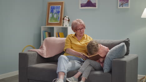 Naughty-little-child-reads-book-with-grandmother-on-sofa