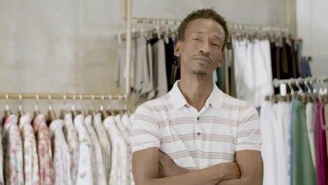 hombre negro barbudo de pie con los brazos cruzados en una tienda de ropa.