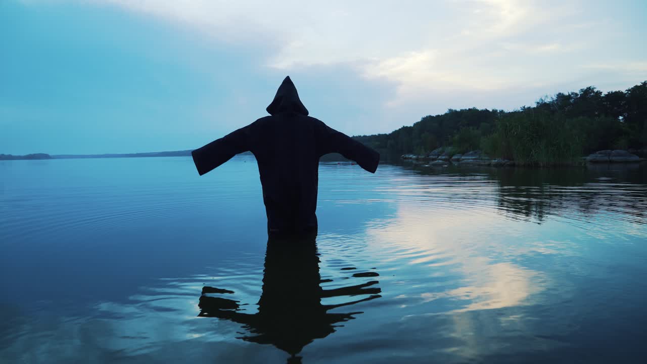 Ghost woman in the water outdoor. Scary figure in black mantle.