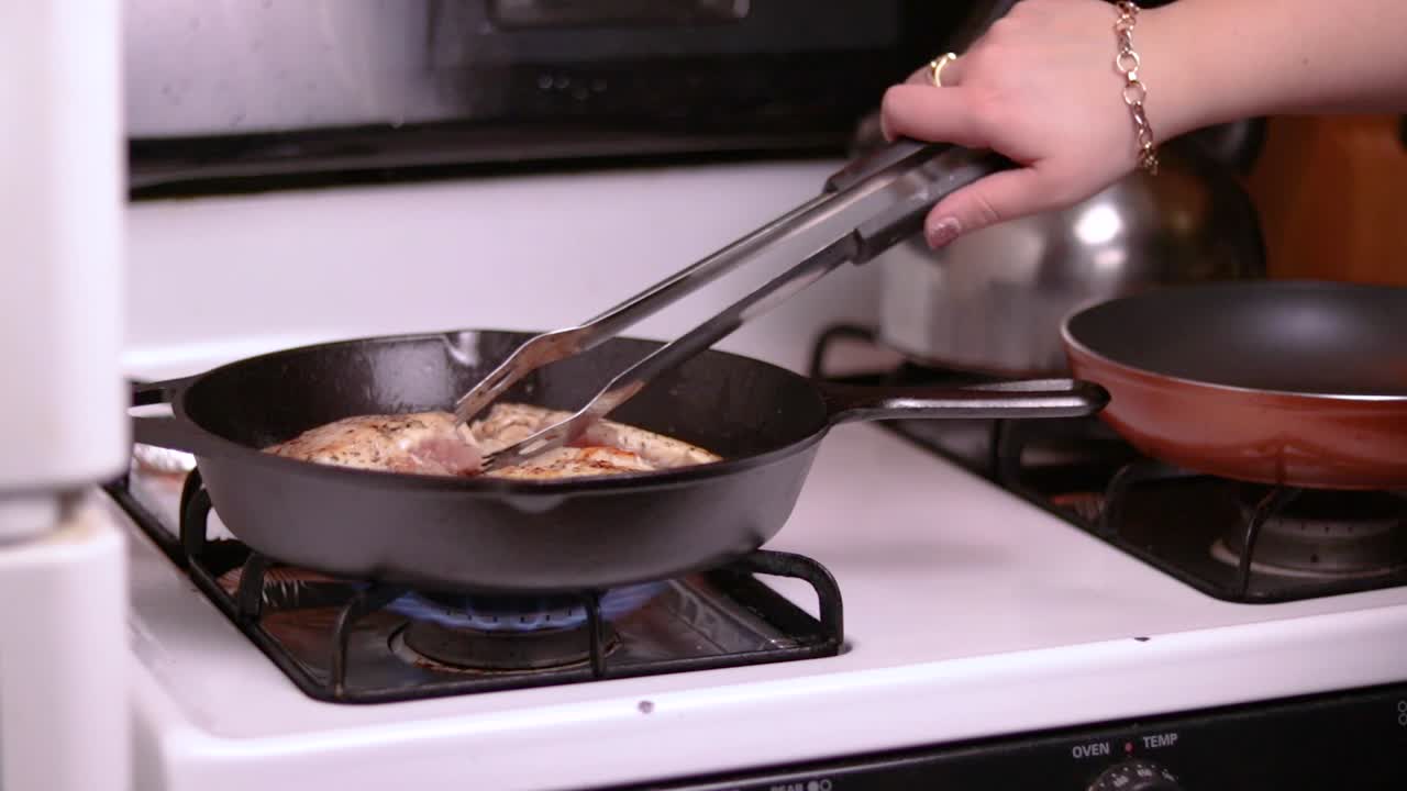 una vista lateral de tres trozos de pechuga de pollo rellenos que se fríen en una sartén forjada encima de una estufa de gas