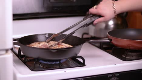 a side view of three pieces of filled chicken breast frying in a forged frying pan on top of a gas stove