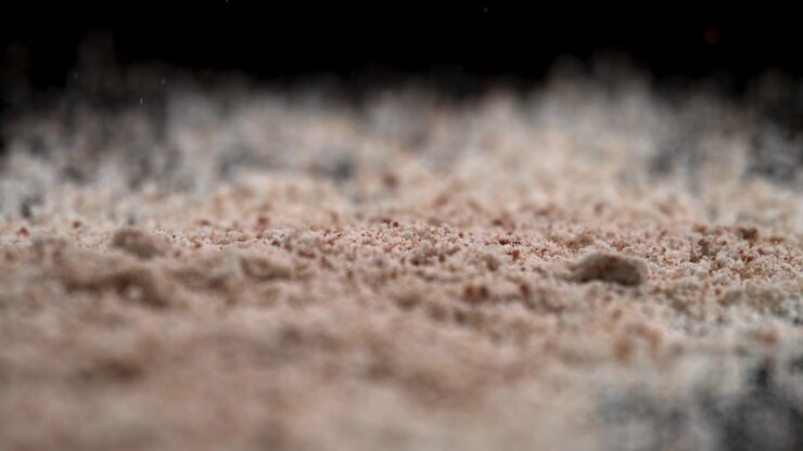 Particelle fini di farina in polvere o trucco cadono e si diffondono su uno sfondo nero luccicante a specchio, in un drammatico macro slow motion.
