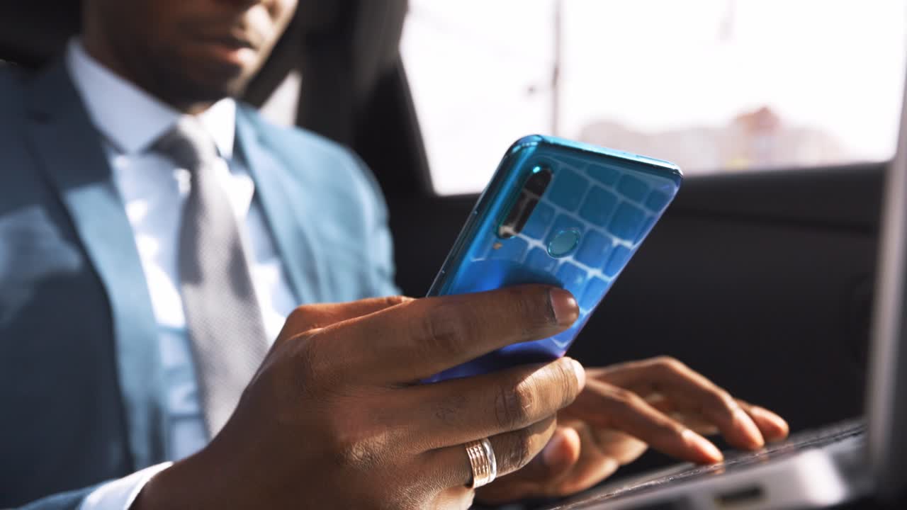 Businessman using smartphone and laptop in a car