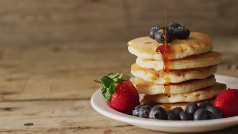 video of maple syrup pouring into pancakes with fruits on wooden background