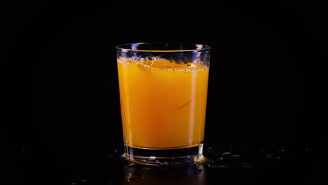 orange juice splashing in a glass on black