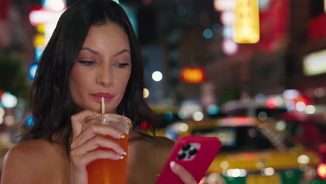 woman enjoying a drink and using phone in a city at night