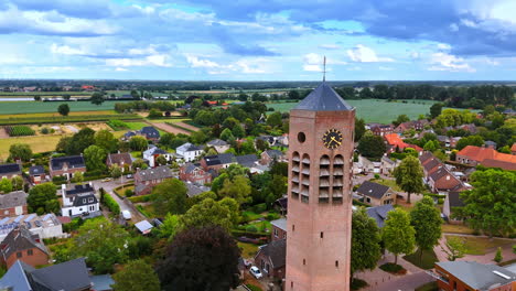 flying around the brick tower with clock with weathercock on top. tower of saint lawrence church in vierlingsbeek, netherlands