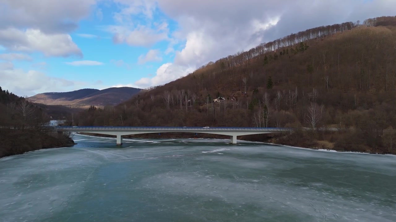 Slovakian Košicen alueella jäätynyt Ružínin tekojärvi sijaitsee metsäisten vuorten ja laaksojen välissä modernin maantiesillan vieressä, nähtynä drone-kuvassa.