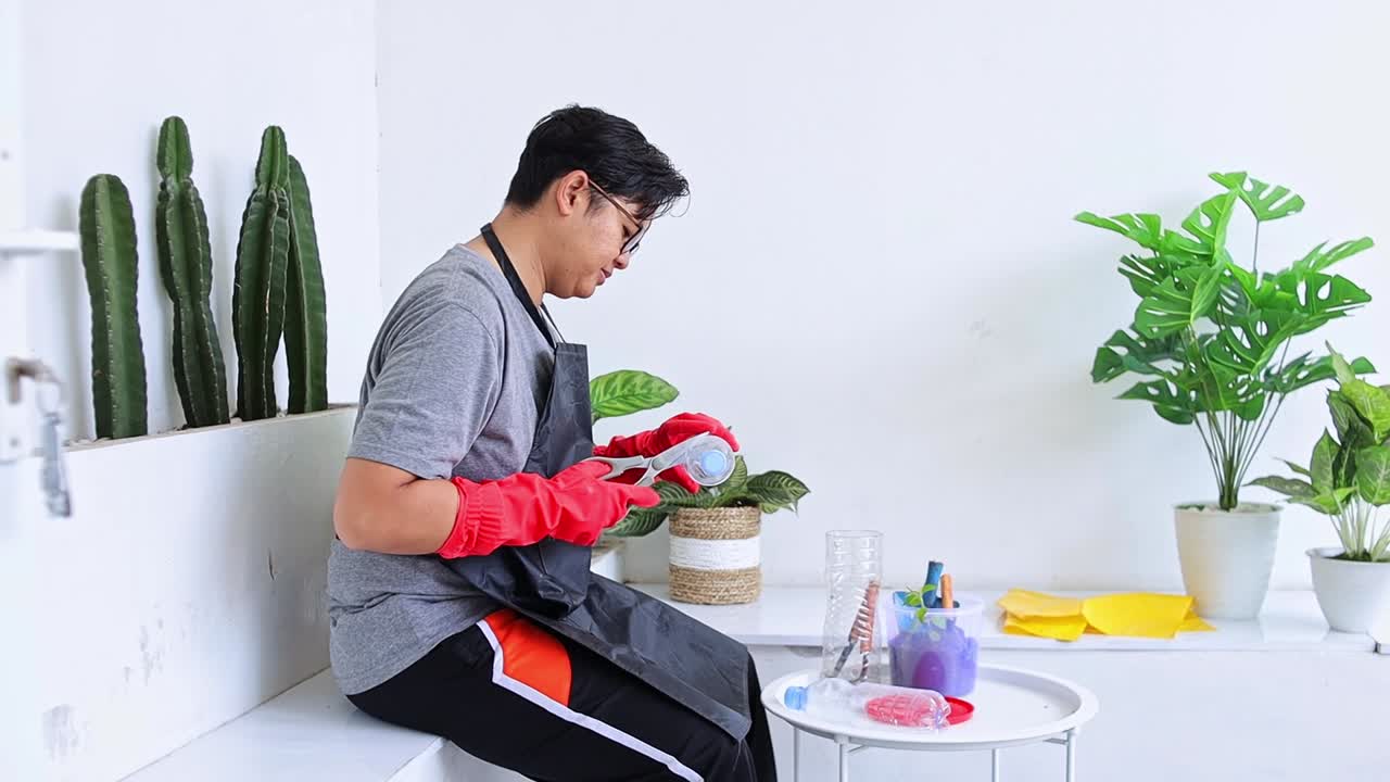 Pria Asia Muda Memotong Botol Bekas untuk Daur Ulang di Halaman