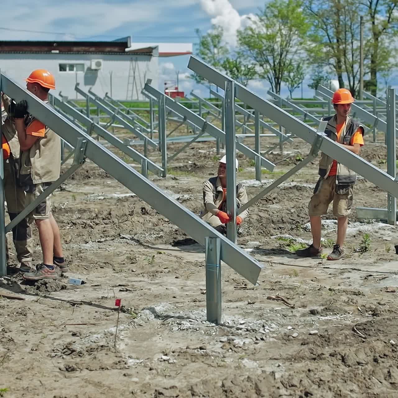 Engineers putting metal construction on the ground. Group of workers in hard hats build metal basis for solar panels on the field in summer day.