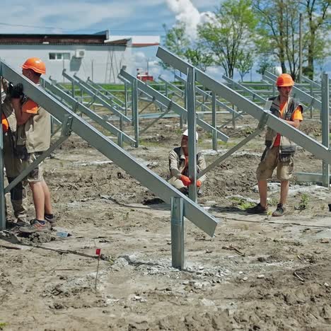 engineers putting metal construction on the ground. group of workers in hard hats build metal basis for solar panels on the field in summer day.