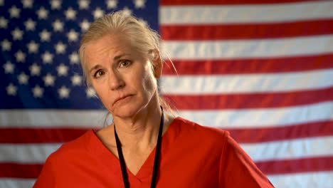 medium tight portrait of nurse looking extremely worried and sad with american flag behind her